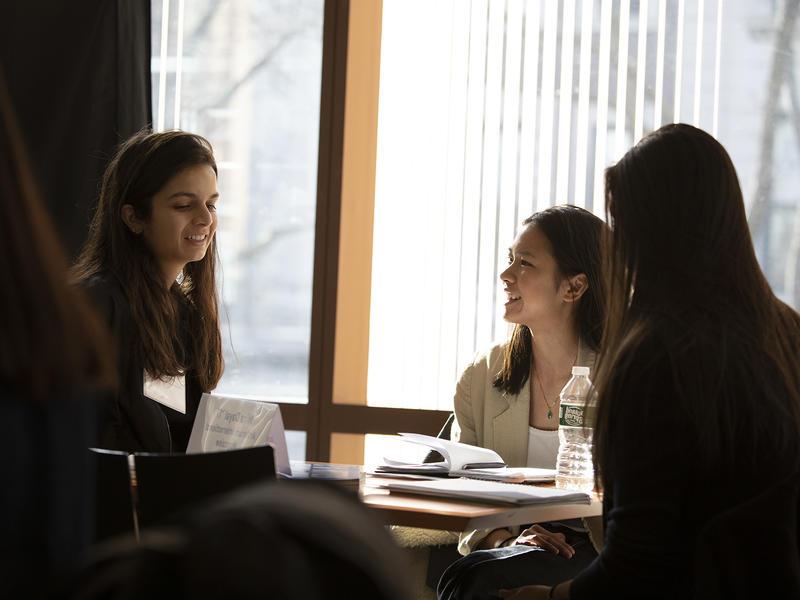 Two students listen as alumna smiles and chats.